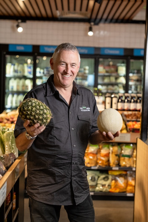 Man holding a pineapple and a melon in a grocery store