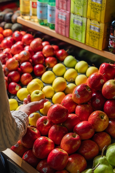 Apples on a market stall with a person's hand reaching for an apple.
