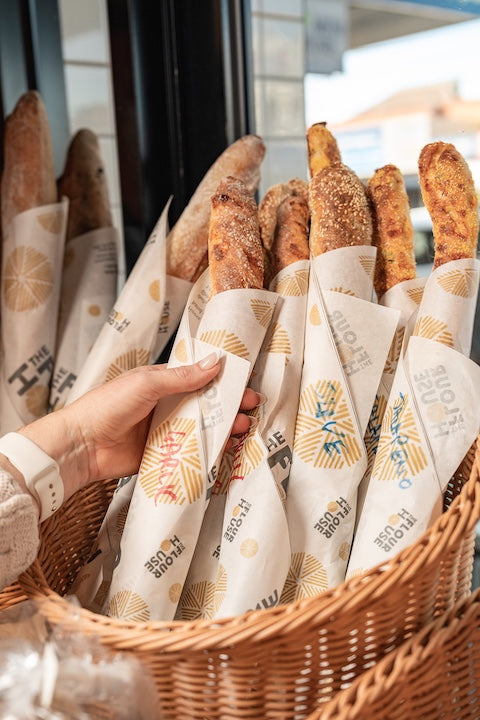Basket of bread wrapped in paper with a hand reaching for one of the loaves.