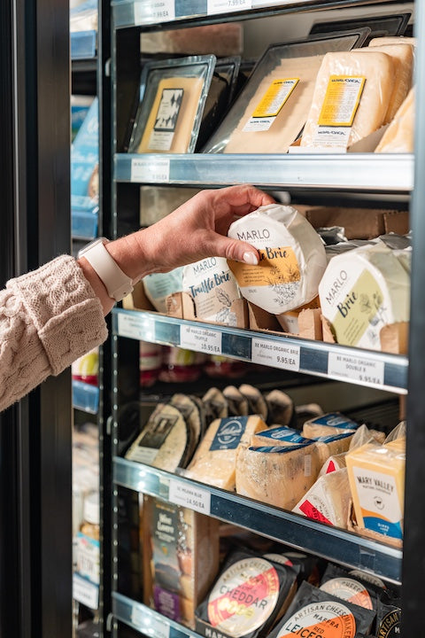 Hand reaching into a refrigerator to grab a package of cheese from a shelf.
