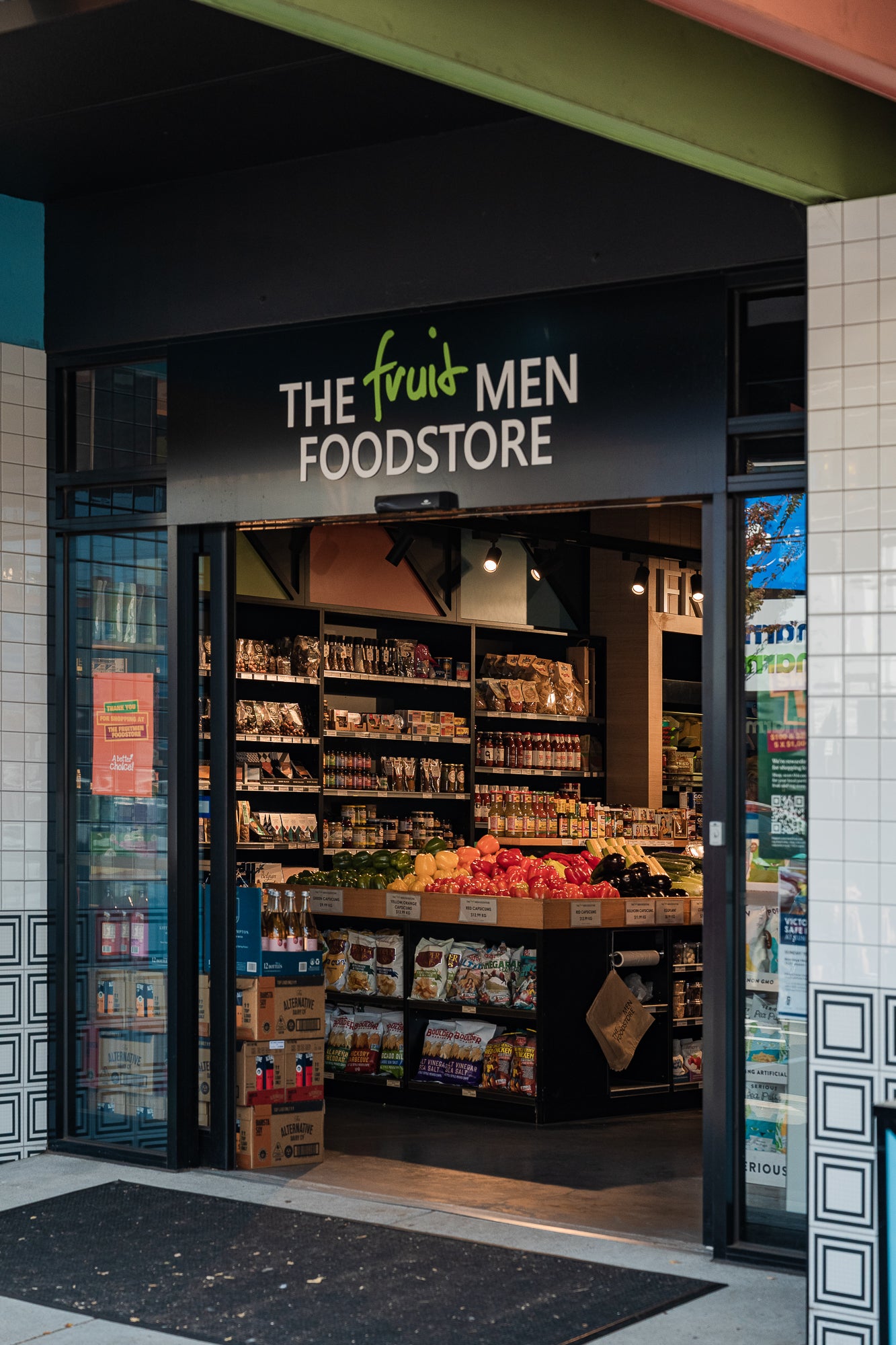 Front entrance of a store named 'The Fruit Men Foodstore' with shelves stocked with products.
