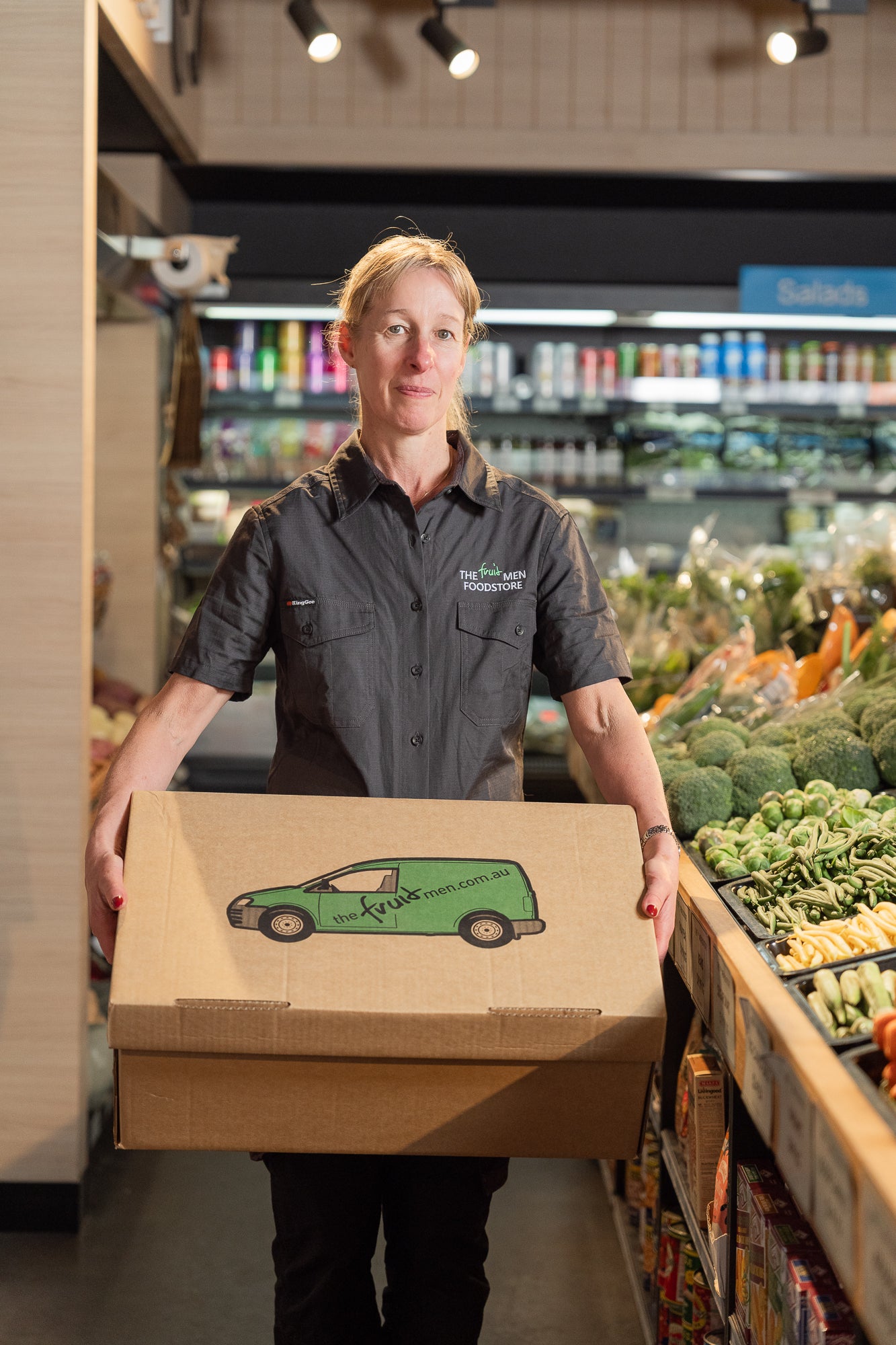 Person holding a box with a green delivery van design in a grocery store.