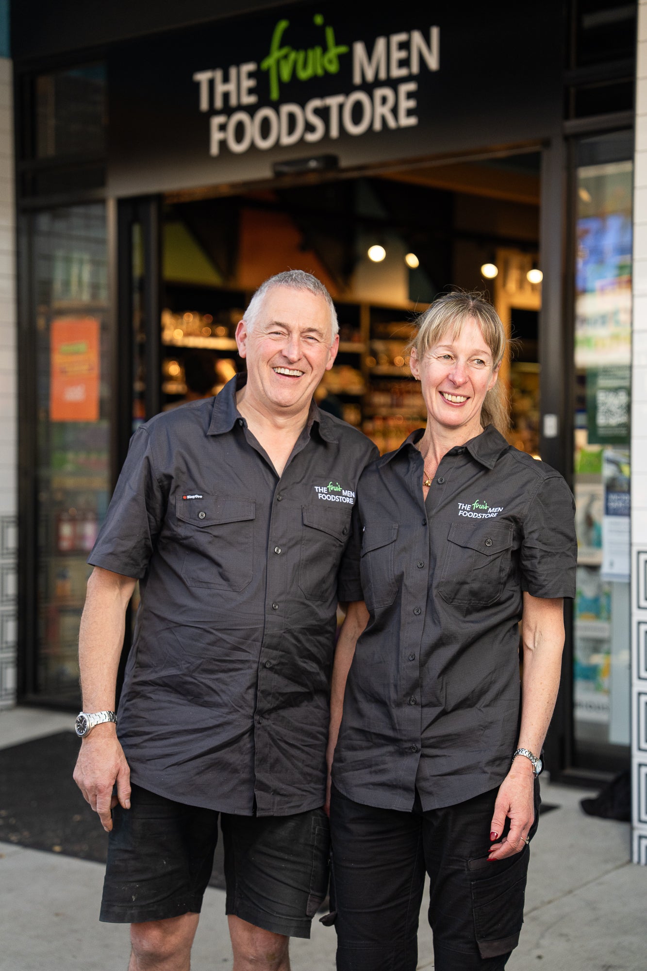 Two people wearing black shirts with logos standing in front of a store.