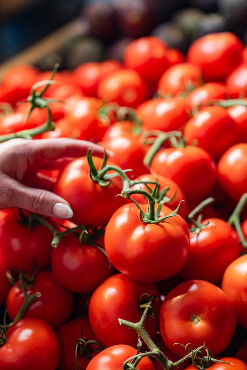 Hand picking a red tomato from a pile of tomatoes on a market stall